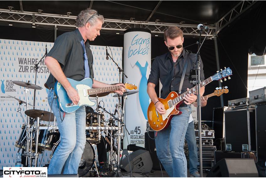 Zwei Gitarrenspieler von der Coverband "Emma Peal" die auf der Bühne stehen und spielen.