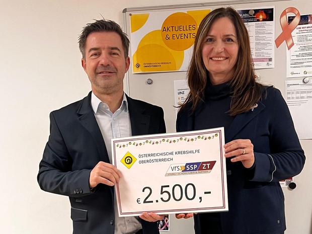 DI Thomas Fellner und GF Maria Sauer posieren mit einem Spendenscheck