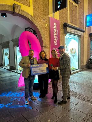 Von Links: Michael Hanisch, Monika Hartl (Beraterin), Nicole Hüttner, Markus Kirnbauer vor der Stadtliebe bei der Spendenchecküberreichung. Im Hintergrund sieht man die Pink Ribbon Schleife als Blow-Up.