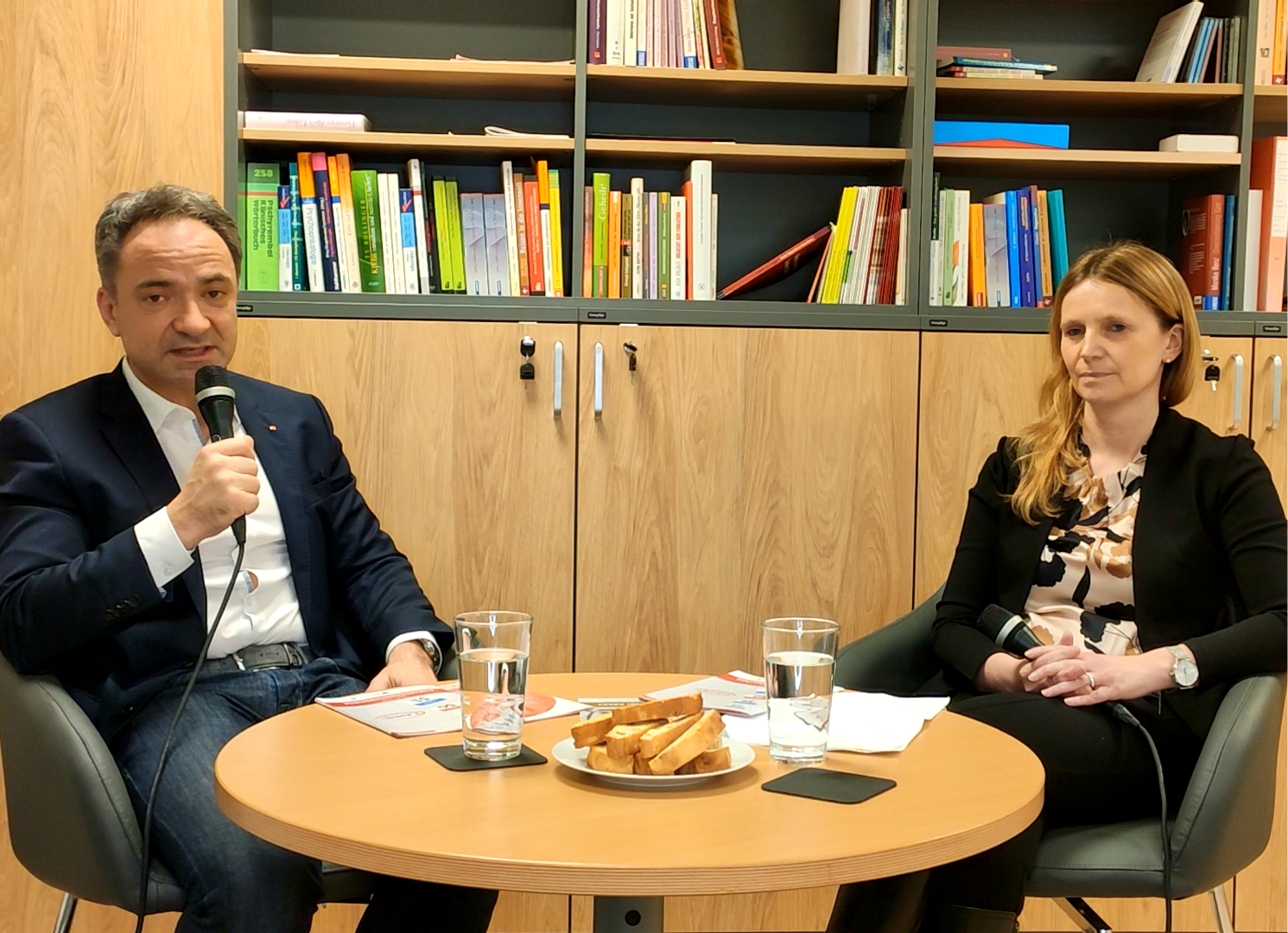 Doz. Dr. Andreas Shamiyeh und Dr. Gudrun Piringer sitzen vor einen kleinen Tisch und halten jeweils ein Mikrofon in der Hand.