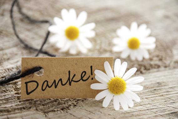 Drei wei&szlig;e Margeriten (Blumen) liegen auf einem Holz. Ein Kartonk&auml;rtchen mit der Aufschrift "Danke" steht neben ihnen. 