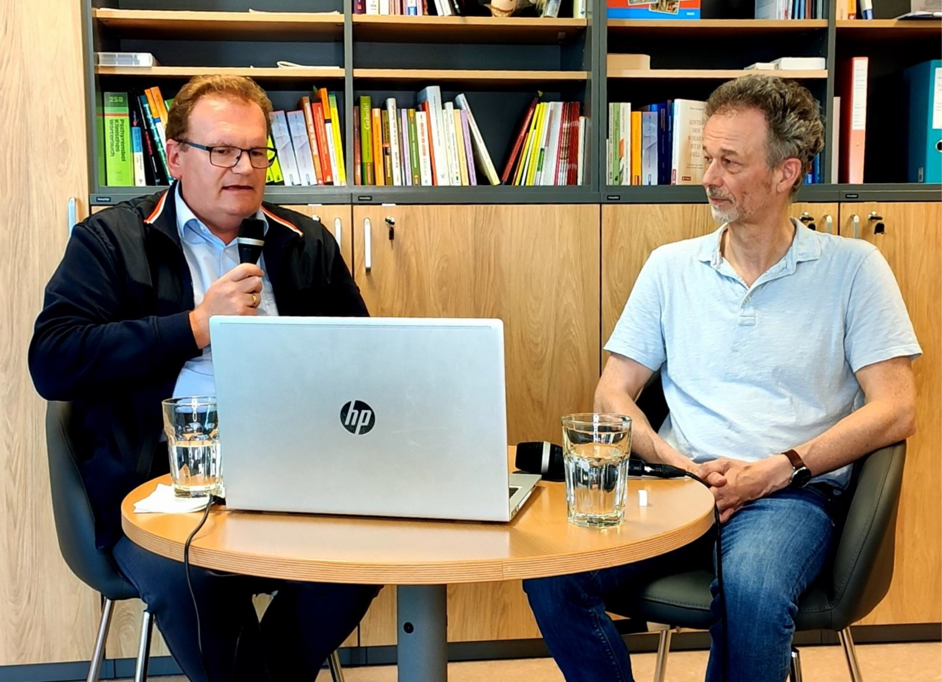 Prim. Univ.-Prof. Mag. Dr. Micael Gabriel und Prim. Univ.-Prof. Dr. Hans Geinitz sitzen vor einen Laptop der auf einen kleinen Tisch steht und beantworten Fragen.