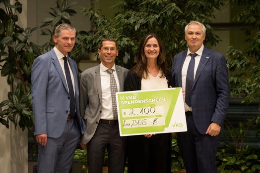 Die Vertreter der PVA überreichen den Spendenscheck über 2.100 Euro an die Organisatoren der Veranstaltung. Die Übergabe findet in einem festlichen Rahmen statt, umgeben von grünen Pflanzen und einer angenehmen Atmosphäre.