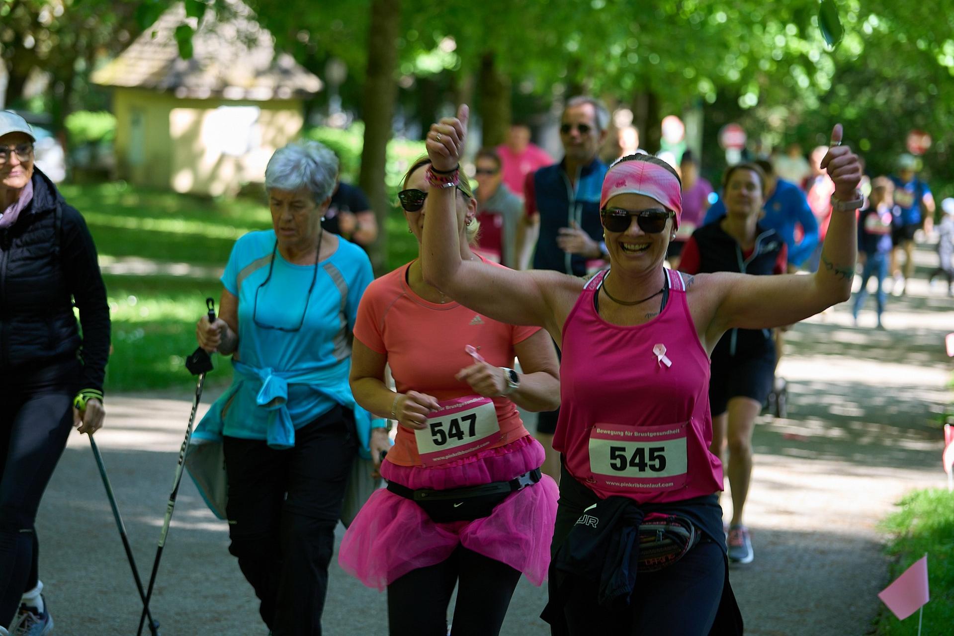 Gruppe von Läuferinnen und Spaziergängern bei einem Lauf-Event in einem grünen Park an einem sonnigen Tag.