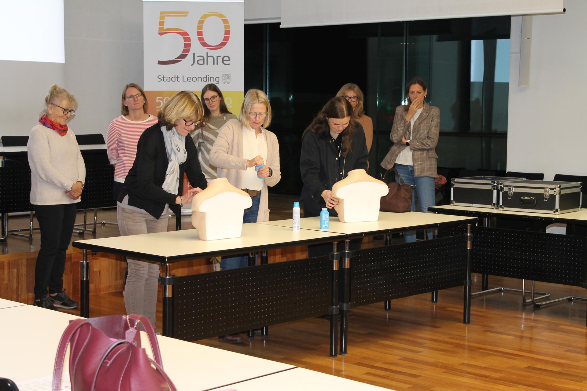 Das Bild zeigt Teilnehmerinnen eines Brusttastseminars in Leonding, bei dem Frauen lernen, wie sie ihre Brüste regelmäßig auf Veränderungen abtasten können. In der praktischen Übung verwenden die Teilnehmerinnen Modellbrüste, um das Erkennen von möglichen Auffälligkeiten zu üben..