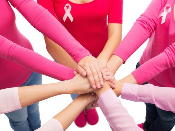 Übereinander liegende Hände von Frauen, die ein rosa langes Shirt tragen worauf die Pink Ribbon Schleife angemacht ist.